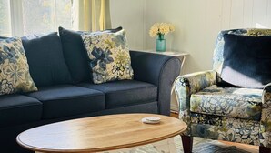 Een woonkamer met een donkerblauwe bank, een gestreept fauteuil, een houten salontafel en een bloemschilderij aan de muur.