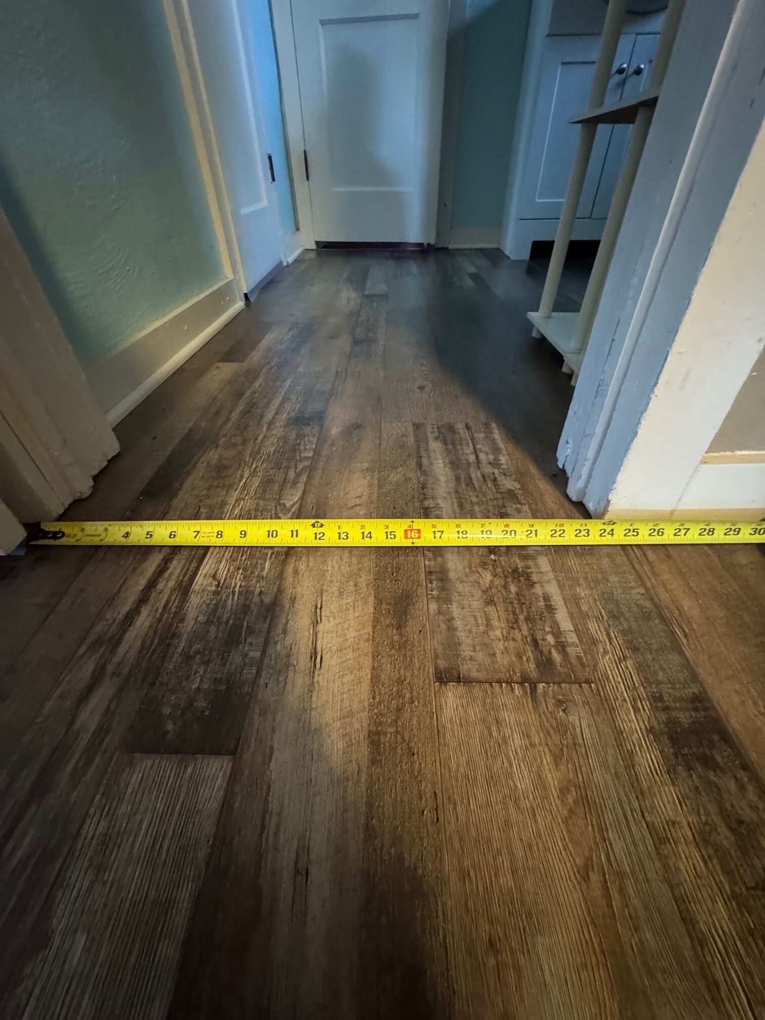 A hallway with wooden flooring and a yellow measuring tape laid across it.