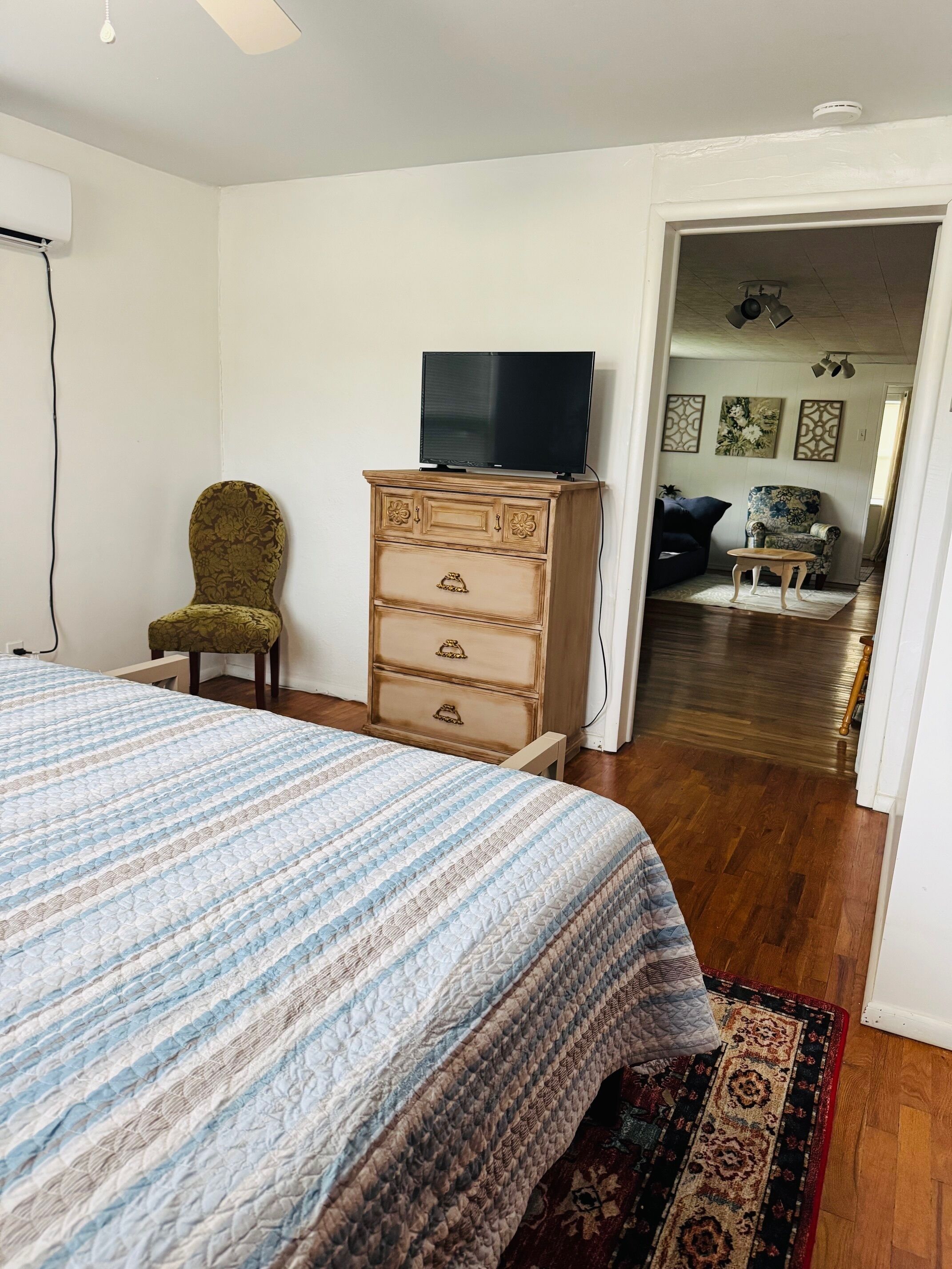 Une chambre à coucher comprenant un lit, une commode, une chaise, un téléviseur et un couloir menant à une autre pièce.