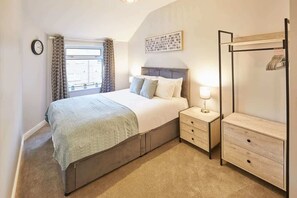 Une chambre à coucher comprenant un lit, des tables de chevet, une armoire, une fenêtre avec des rideaux et une horloge murale.