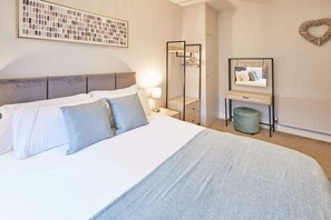 Une chambre d’hôtel bien rangée, avec un lit, un miroir, un radiateur et une œuvre d’art encadrée accrochée au mur.