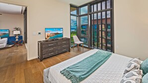 Ein Schlafzimmer mit großem Fenster, einem Bett mit grüner Decke, einem Schminktisch und einem Stuhl.