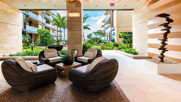 Eine moderne Lobby mit Korbmöbeln, einem zentralen Couchtisch und Blick auf die umliegende Natur und Gebäude.