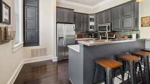 A modern kitchen with dark cabinets, stainless steel appliances, and a central island with bar stools. - Game Day Getaway - 1 Block to Dickson-Walk to UofA (Fayetteville)