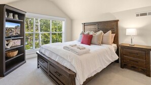A bedroom with a large window, a bed with white bedding, a wooden headboard, a nightstand with a lamp, and a bookshelf with decorative items. - Game Day Getaway - 1 Block to Dickson-Walk to UofA (Fayetteville)