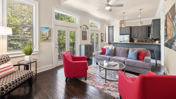 A spacious living room with a grey sofa, red armchairs, and a coffee table. There is a kitchen area with grey cabinets and a dining table. - Game Day Getaway - 1 Block to Dickson-Walk to UofA (Fayetteville)