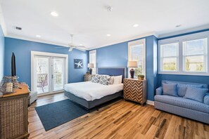 Um quarto com uma cama, mesa de cabeceira, cômoda, janela com persianas e ventilador de teto.
