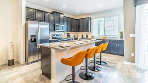 A modern kitchen with dark cabinets, a stainless steel refrigerator, a microwave, and a large island with bar stools. - Private Pool Townhome Near Disney Parks (Kissimmee)