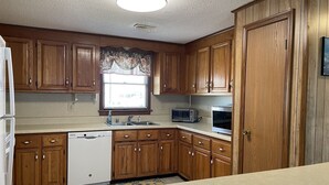 A kitchen with wooden cabinets, a dishwasher, a microwave, and a window with a floral valance. - Southern Star 5 Bedroom Cottage by RedAwning (Hatteras)