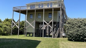 A multi-story building with a wooden framework, a balcony on the upper floor, and a staircase leading to the entrance. - Southern Star 5 Bedroom Cottage by RedAwning (Hatteras)