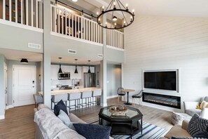 A spacious living room with a high ceiling, a fireplace, and a kitchen area with a bar.