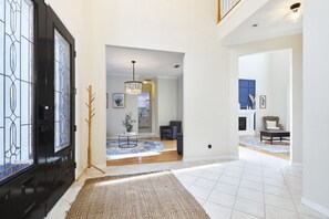 A spacious hallway with a black door, a rug, and a dining area with a chandelier. - The Oasis Retreat +Pool +Game Room +Basketball + Massive Yard +Near Beach & Golf (Largo)