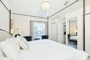 A bedroom with a four-poster bed, a chandelier, a window with curtains, and a door leading to another room. - The Oasis Retreat +Pool +Game Room +Basketball + Massive Yard +Near Beach & Golf (Largo)