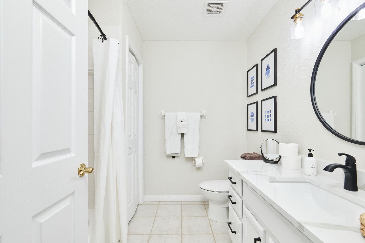A bathroom with a toilet, sink, and mirror. There are towels hanging on the wall and a shower curtain.