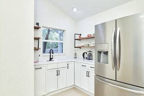 A modern kitchen with white cabinetry, a stainless steel refrigerator, and a window with a view of trees. - The Oasis Retreat +Pool +Game Room +Basketball + Massive Yard +Near Beach & Golf (Largo)