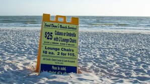 A beachside sign advertising beach services including a $25 option for a cabana or umbrella with lounge chairs, and lounge chairs for $8 each or 2 for $15. - The Oasis Retreat +Pool +Game Room +Basketball + Massive Yard +Near Beach & Golf (Largo)