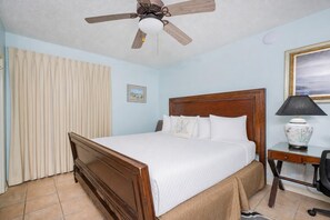 Une chambre d’hôtel avec un lit en bois, un ventilateur de plafond, un bureau avec une lampe et un tableau au mur.