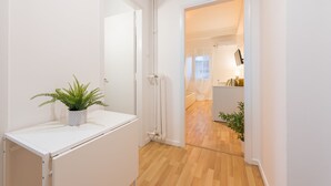 A narrow hallway with a white radiator, a potted plant, and a wooden floor leading to a room with a bathtub and a mirror. - Apartment at Megaro Mousikis metro station 1bed 2 pers (Athens)