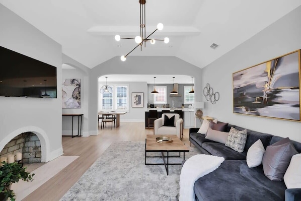 A spacious living area with a fireplace, a sofa, a coffee table, and a dining area in the background.