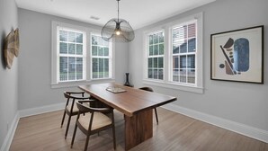 A dining area with a wooden table and chairs, large windows with blinds, a hanging light fixture, and a framed abstract artwork on the wall. - San Marco Chic Home 2 blocks from San Marco Square (Jacksonville)
