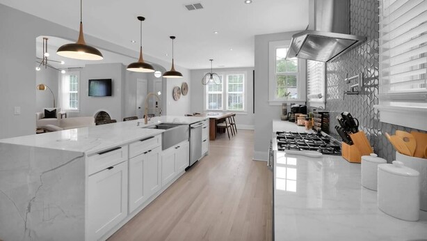 A modern kitchen with white cabinetry, a large island, pendant lighting, and a view of the dining area. - San Marco Chic Home 2 blocks from San Marco Square (Jacksonville)