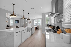 A modern kitchen with white cabinetry, a large island, pendant lighting, and a view of the dining area.