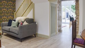 A living room with a grey sofa, a wooden staircase, and a stone wall. - 2 bedroom accommodation in Abererch (Abererch)