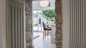 A stone archway leading to a dining area with a table and chairs, a hanging light fixture, and a view of the outdoors. - 2 bedroom accommodation in Abererch (Abererch)