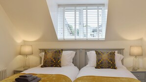 A twin bed with a yellow throw blanket and two pillows, a bedside table with a lamp, and a window with blinds. - 2 bedroom accommodation in Abererch (Abererch)