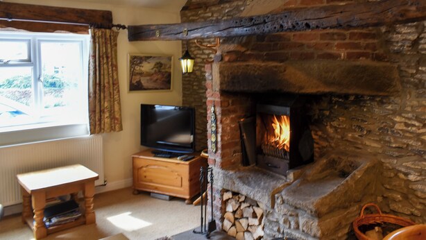 A cozy living room with a stone fireplace, a television on a wooden cabinet, and a window with curtains. - 1 bedroom accommodation in Gillamoor, near Kikbymoorside (Gillamoor, near Kikbymoorside)