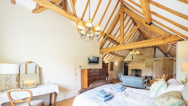 Un dormitorio con techo de madera, una cama, un escritorio, una silla y una chimenea.