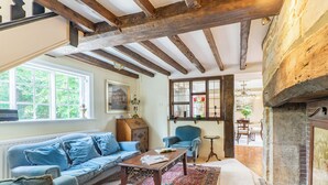Una habitación acogedora con vigas de madera a la vista, una chimenea, un sofá azul y una alfombra estampada.