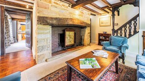 Una habitación con chimenea de piedra, vigas de madera, un sillón azul y una mesa de centro de madera.