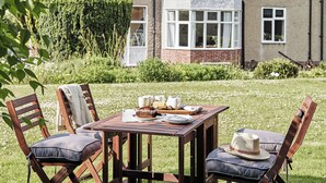 Una mesa de madera al aire libre con sillas, una cesta y un sombrero.