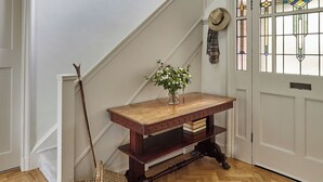 Un banco de madera con un jarrón de flores, una cesta de mimbre y un sombrero en la pared.