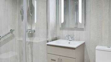 A modern bathroom with a glass-enclosed shower, a white sink, and a toilet.