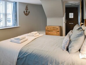 A neatly made bed with folded towels, a wooden headboard, and a patterned pillow. - A unique cottage in a fabulous seaside village. (Portpatrick)