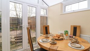 A round wooden dining table with four chairs, a glass of juice, croissants, and a coffee pot. - Maple Cottage (Broadway)