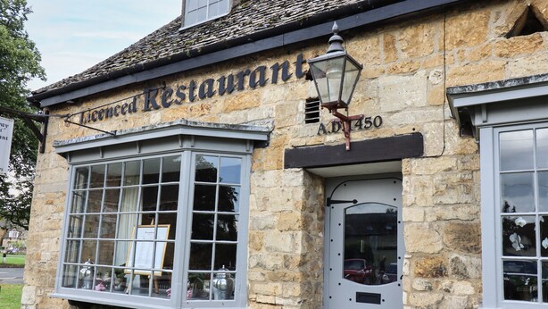 A stone building with a sign reading "Licensed Restaurant" and a window displaying various items. - Maple Cottage (Broadway)