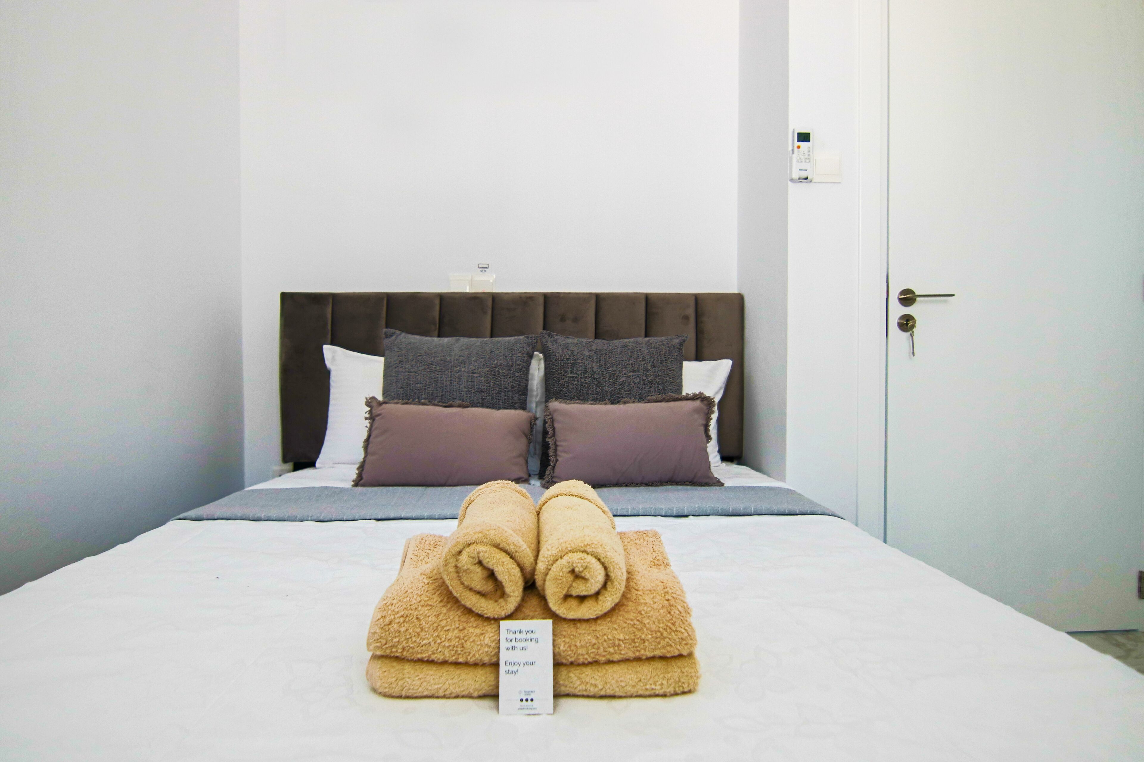 A neatly made bed with rolled towels, a headboard, and a sign on the bed.
