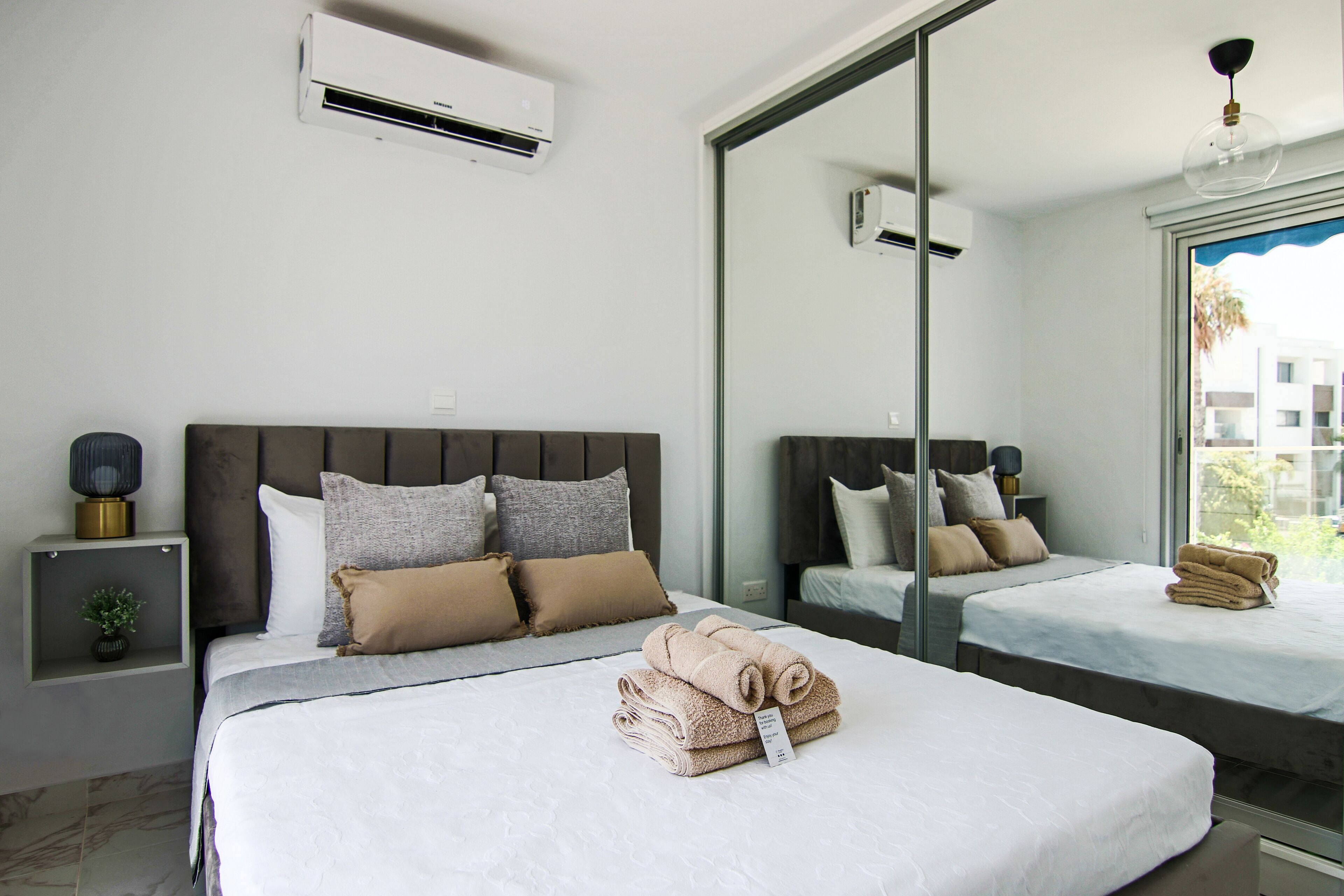 Une chambre d’hôtel moderne avec un grand lit, un lit plus petit et un miroir qui reflète la pièce.