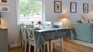 A dining area with a table set for four, white chairs, a window with a view of trees, and framed pictures on the wall. - The Butchers Cottage (Edzell, near Brechin)