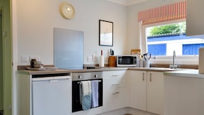 A modern kitchen with white cabinetry, a built-in oven, a microwave, and a window with striped curtains. - The Butchers Cottage (Edzell, near Brechin)
