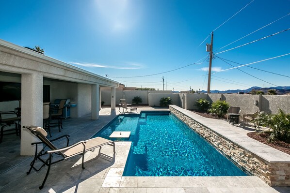 Piscina com borda de pedra, rodeada por espreguiçadeiras e um espaço coberto com varanda.