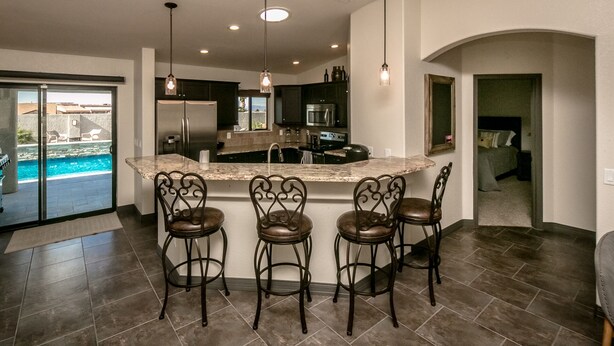 A modern kitchen with a central island, bar stools, and a view of a swimming pool. - Free Heated Pool, RV Garage, Hot Tub, Music, Views (Lake Havasu City)