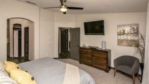 A bedroom with a bed, a dresser, a chair, a ceiling fan, a TV, and a painting on the wall. - Free Heated Pool, RV Garage, Hot Tub, Music, Views (Lake Havasu City)