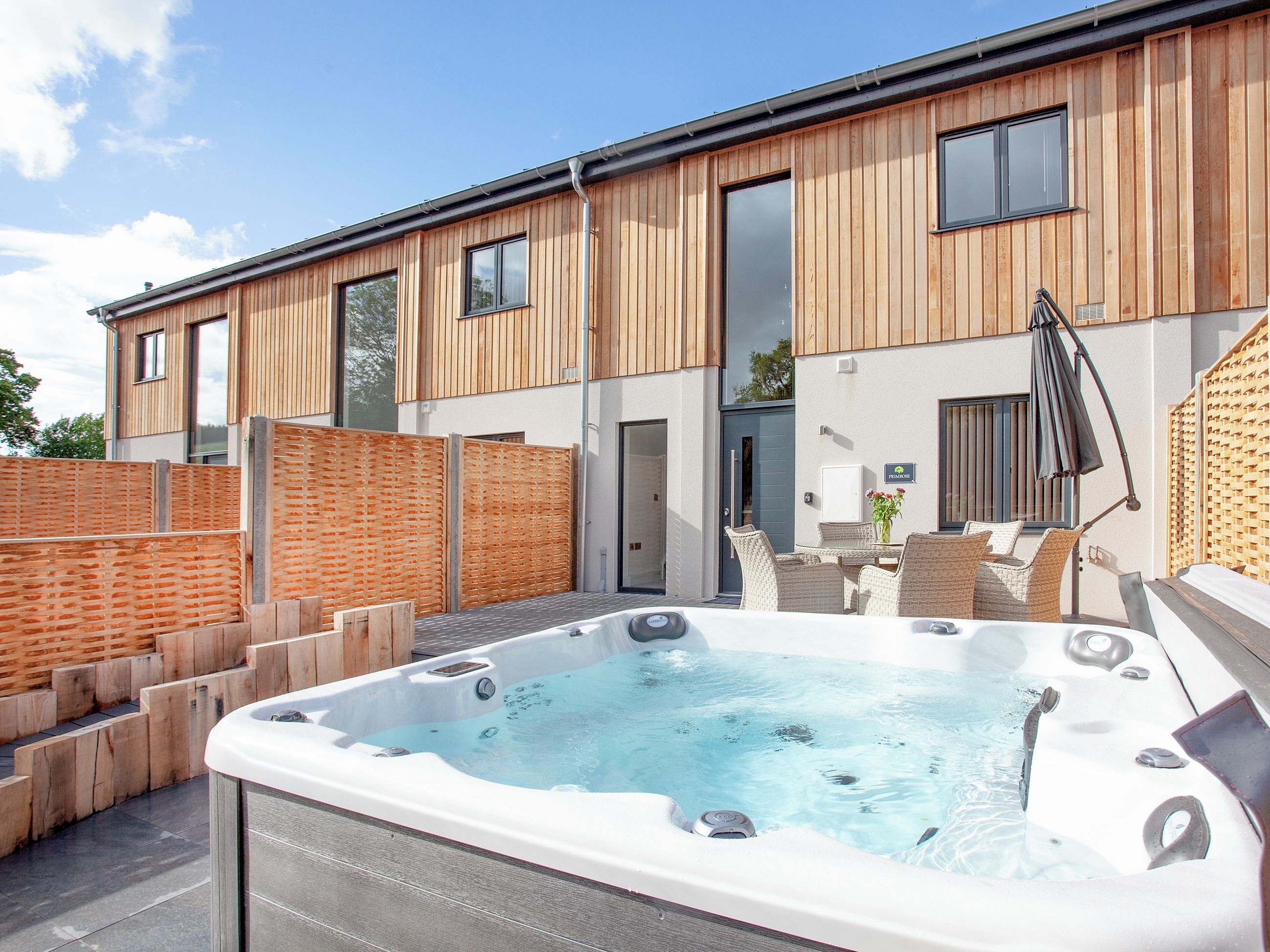 Un bâtiment moderne avec une façade en bois, un jacuzzi et du mobilier d’extérieur.