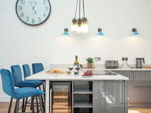 A modern kitchen with a central island, bar stools, a clock, pendant lights, and a toaster.