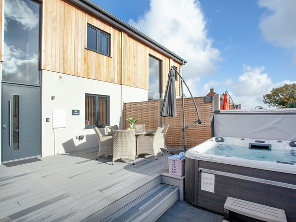 A modern building with a wooden facade, a hot tub, outdoor seating, and a clear sky.
