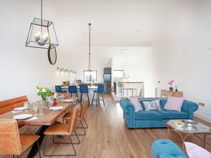 A modern living space with a dining area, a blue sofa, and a kitchen in the background.